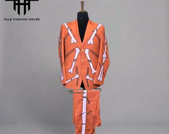 Op de afbeelding: Oranje pak met een wit bottenpatroon, gepresenteerd op een mannequin. Het pak bestaat uit een blazer en een bijpassende broek. De blazer heeft een revers en een knoopsluiting. De broek heeft een rechte pijp. Het pak is van FULE FASHION HOUSE.