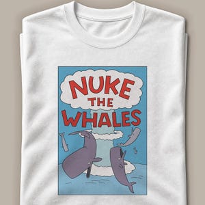 Könnte beinhalten: Ein weißes T-Shirt mit Rundhalsausschnitt und einem Grafikdruck einer blauen Ozeanszene mit einem Atompilz und dem roten Text NUKE THE WHALES. Mehrere graue Wale schwimmen in dieser Cartoon-Illustration im Wasser unter der Wolke.