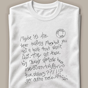 May include: A white crew neck t-shirt featuring black handwritten-style text that reads: Maybe it's the beer talking Marge but you got a butt that won't quit. they got those big chewy pretzels here five dollars ?!?!!? get outta here. A circular stamp reads Springfield 1978.
