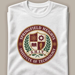 May include: A white crew neck t-shirt featuring a circular maroon and gold emblem. The emblem displays a shield with an atom, gear, book, and torch, surrounded by green laurel leaves and the text Springfield Heights Institute of Technology S.H.I.T.