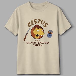 May include: Beige t-shirt featuring a cartoon illustration of Cletus Spuckler with a rifle and a can of beer. The text on the shirt reads "CLETUS THE SLACK-JAWED YOKEL".