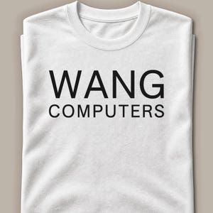 Può includere: Una t-shirt bianca a maniche corte con il testo nero WANG COMPUTERS stampato in un carattere sans-serif in grassetto al centro del petto. Il capo presenta un classico girocollo ed è piegato ordinatamente per mostrare chiaramente la grafica.