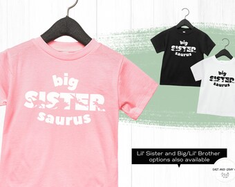 Op de afbeelding: Roze, zwarte en witte T-shirts met de tekst "big sister saurus" erop gedrukt. De tekst is gemaakt van dinosaurus silhouetten.