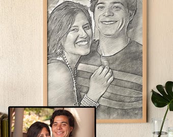 May include: A framed pencil sketch portrait of a smiling couple, with a smaller framed photograph of the same couple below. The sketch is in a light wooden frame. The photograph is in a black frame. The background is a neutral beige.