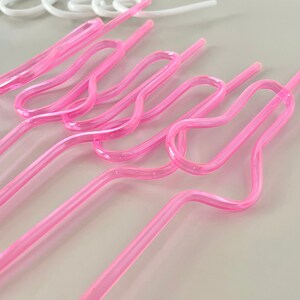 May include: Several pink, curved plastic straws are arranged diagonally across the frame. The straws have a unique, looped design in the middle. A few white straws are visible in the background.
