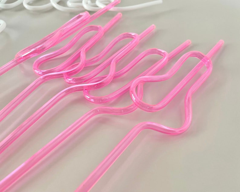 May include: Several pink, curved plastic straws are arranged diagonally across the frame. The straws have a unique, looped design in the middle. A few white straws are visible in the background.