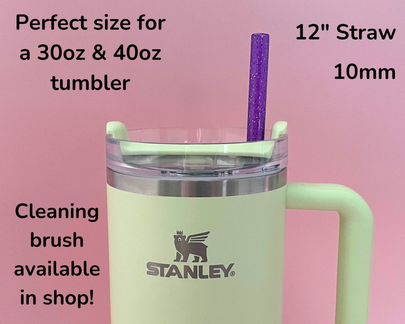 May include: A green 30oz or 40oz Stanley tumbler with a lid and a handle. The tumbler has a silver band around the middle and the Stanley logo is visible. A purple 12-inch straw with glitter is inserted into the tumbler.