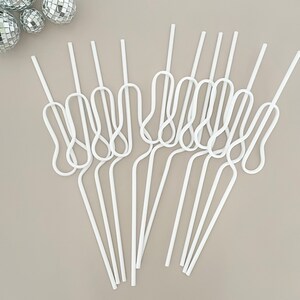 May include: A collection of white, looped straws arranged on a neutral background. The straws have a unique design with a curved, figure-eight shape in the middle. Silver disco balls are in the upper left corner. The straws are made of a flexible material.
