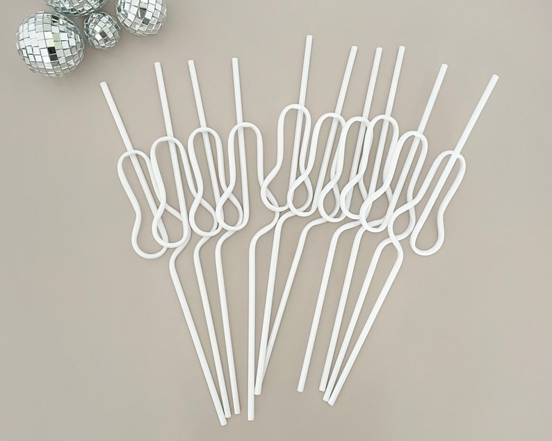 May include: A collection of white, looped straws arranged on a neutral background. The straws have a unique design with a curved, figure-eight shape in the middle. Silver disco balls are in the upper left corner. The straws are made of a flexible material.