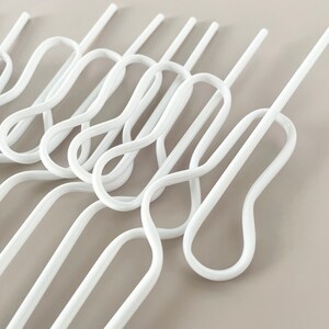 May include: A collection of white, wavy-shaped hangers. The hangers have a unique design with a series of loops and straight sections, creating an interesting visual pattern. The hangers are made of a smooth, glossy material.