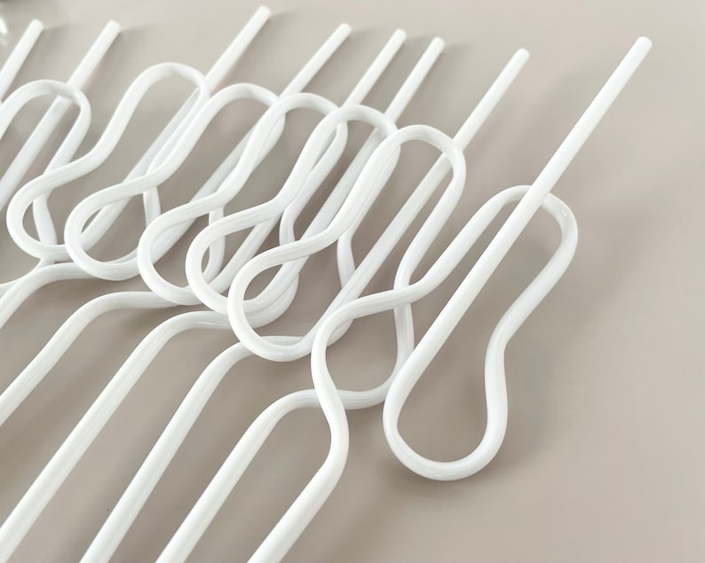 May include: A collection of white, wavy-shaped hangers. The hangers have a unique design with a series of loops and straight sections, creating an interesting visual pattern. The hangers are made of a smooth, glossy material.
