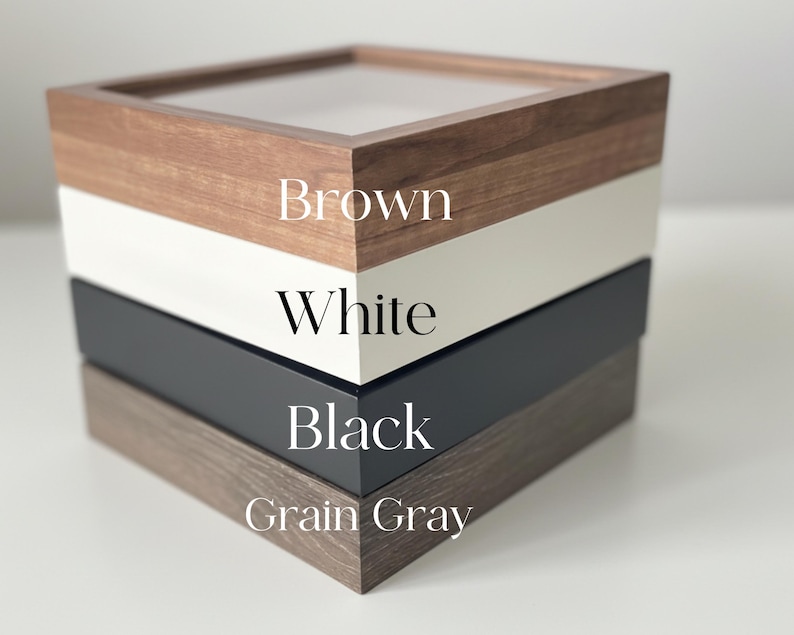 May include: A square wooden box with a clear top, featuring layers of brown, white, black, and grain gray. The text on the side of the box indicates the color of each layer.