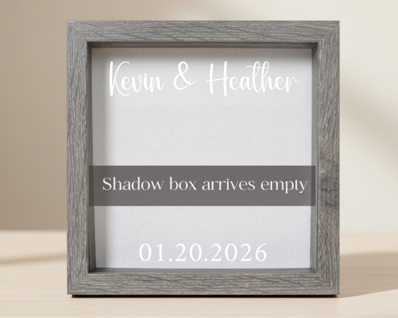 May include: A gray wooden shadow box frame with white text that reads "Kevin & Heather", "Shadow box arrives empty", and the date "01.20.2026". The frame has a light gray background.