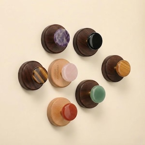 May include: A selection of decorative wooden knobs featuring gemstone accents like amethyst, onyx, tiger's eye, rose quartz, jade, and red jasper. The knobs are set on dark wood bases, with one bearing the text "CUSTOM AFFORDABLE".