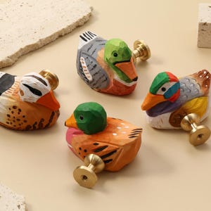 May include: Four hand-painted wooden duck-shaped cabinet knobs with brass fittings. The ducks are painted in vibrant colours including orange, green, blue, and white. Decorative hardware for drawers, cabinets, or furniture.
