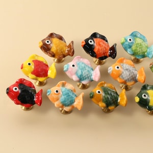 May include: A collection of eleven colorful ceramic fish-shaped cabinet knobs. Each knob features a unique color scheme, including red, yellow, blue, orange, and green, with gold-toned metal bases. These decorative knobs add a whimsical touch.