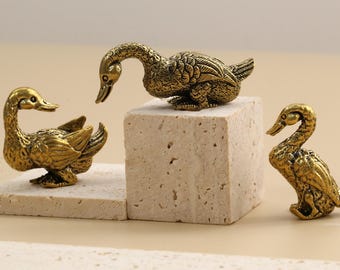 May include: Three antique brass duck figurines. One duck stands on a small rectangular block, another on a square block, and the third on a flat surface. The ducks have detailed feather textures and are in various poses.
