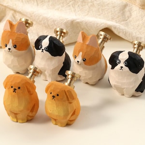 May include: Six wooden cabinet knobs, each shaped like a dog. The dogs are painted in orange, black, and white. Each knob has a brass-coloured metal stem. The knobs are designed for use on cabinets or drawers.