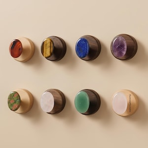 May include: A collection of eight decorative knobs. Each knob features a different gemstone set in a wooden base. Gemstones include red, yellow, blue, purple, green, and pink. The knobs are mounted on a light beige wall.