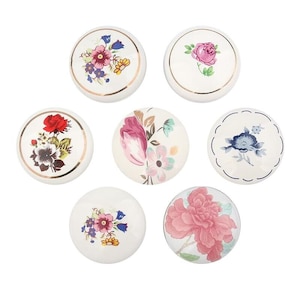 May include: Six white ceramic knobs with different floral designs. The knobs have a gold trim around the edge.