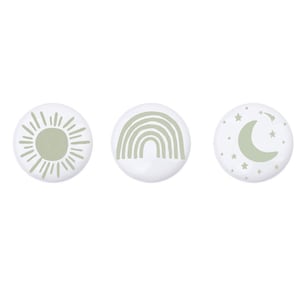 Może przedstawiać: Trzy białe okrągłe naklejki z zielonymi wzorami. Pierwsza naklejka ma słońce z promieniami. Druga naklejka ma tęczę. Trzecia naklejka ma półksiężyc z gwiazdami.