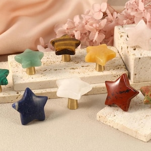 May include: A selection of star-shaped cabinet knobs in various colours and materials, including green malachite, blue lapis lazuli, and red jasper. Each knob has a brass base. Decorative furniture hardware.