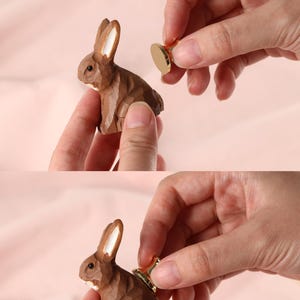 May include: A brown wooden rabbit figurine with white-tipped ears. A gold-coloured knob is being installed by hand. The text "All knobs are installed by hand" is at the top of the image.