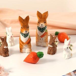 Könnte beinhalten: Ein Set aus sieben Holz-Hasenfiguren, einige halten Karotten. Die Hasen sind in verschiedenen Farben bemalt, darunter Weiß, Braun und Orange. Die Figuren eignen sich perfekt zum Dekorieren eines Hauses oder zum Hinzufügen eines Hauches von Verspieltheit zu einem Regal.
