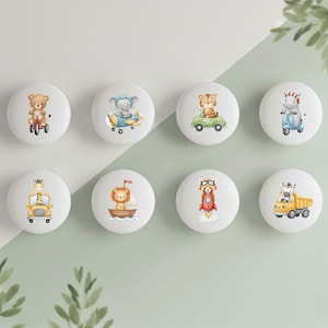 May include: Eight white cabinet knobs with colorful illustrations of animals on vehicles. The animals include a bear on a tricycle, an elephant in a plane, a tiger in a car, and a zebra on a scooter.