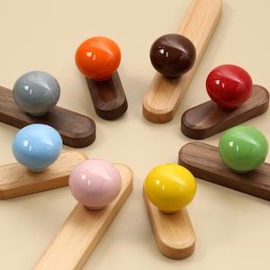 May include: A selection of colourful spherical knobs in shades of orange, brown, red, green, yellow, pink, blue, and grey. Each knob is mounted on a wooden base, with some bases being lighter wood and others darker wood.