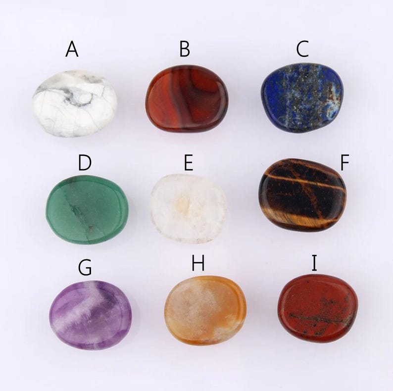 May include: Nine polished gemstones in a variety of colours and patterns are displayed. The stones include white, red, blue, green, cream, brown, purple, orange, and dark red. Each stone has a smooth, rounded shape and is displayed on a white surface.