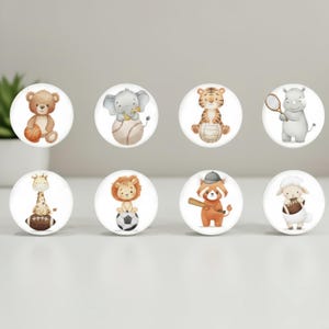 May include: Set of eight round cabinet knobs featuring watercolor illustrations of animals playing sports. Includes a teddy bear with a basketball, an elephant with a baseball, and a tiger with a volleyball.