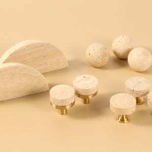 Peut inclure: Un ensemble de quincaillerie décorative dans une palette de couleurs neutres. L'ensemble comprend deux formes en demi-cercle, quatre sphères et six boutons cylindriques avec des bases en laiton. Les articles ont un aspect texturé semblable à de la pierre.