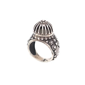 May include: A silver ring with a domed top and intricate detailing. The top of the ring is a cage-like design with small, round accents.