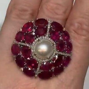 May include: A large ring with a large, white pearl surrounded by a cluster of red rubies and smaller diamonds.