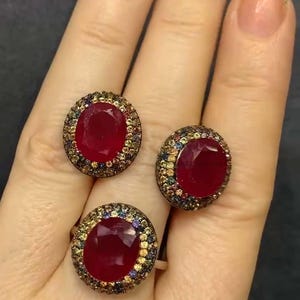 May include: Three silver rings with red oval gemstones surrounded by smaller colorful gemstones.