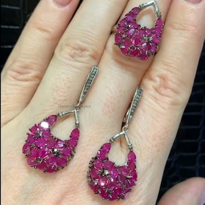 Pode incluir: Um conjunto de brincos e anel de rubi e diamantes. Os brincos têm forma de lágrima e apresentam um cacho de rubis com detalhes de diamantes. O anel também tem forma de lágrima e apresenta um cacho de rubis com detalhes de diamantes.