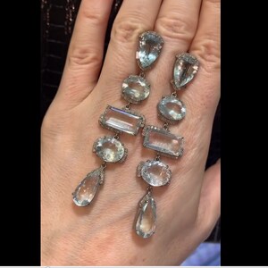 May include: A pair of long, silver dangle earrings with multiple aquamarine gemstones of different shapes and sizes. The earrings are set with small diamonds around the edges of the gemstones.