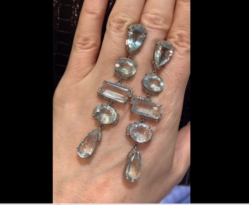 May include: A pair of long, silver dangle earrings with multiple aquamarine gemstones of different shapes and sizes. The earrings are set with small diamonds around the edges of the gemstones.