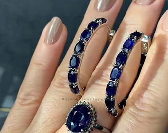 May include: A pair of silver hoop earrings with blue gemstones and a silver ring with a large blue gemstone. The ring has a halo of smaller gemstones around the center stone.