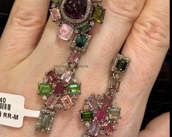 May include: A pair of dangle earrings with a cluster of colorful gemstones, including pink, green, and purple, set in silver. The earrings feature a teardrop-shaped gemstone at the top and a smaller cluster of gemstones at the bottom.
