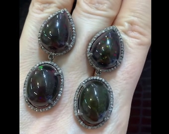 May include: A pair of dangle earrings with black opal gemstones set in silver. Each earring features a pear-shaped opal and a round opal, both surrounded by a halo of small diamonds.