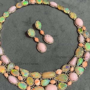 May include: A necklace and matching earrings set featuring a variety of opal gemstones in shades of pink, yellow, and green. The jewelry is set in a silver metal with a diamond-like border, creating a luxurious look.