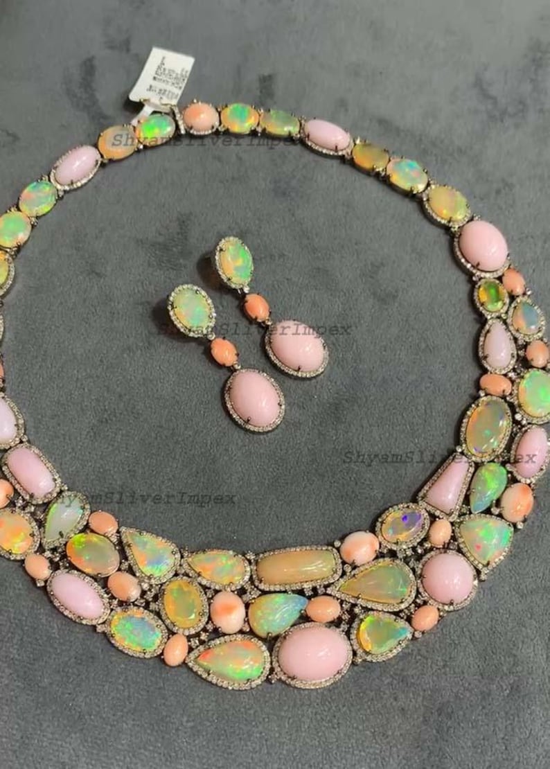 May include: A necklace and matching earrings set featuring a variety of opal gemstones in shades of pink, yellow, and green. The jewelry is set in a silver metal with a diamond-like border, creating a luxurious look.
