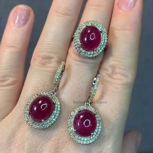 May include: A set of ruby and diamond earrings and ring. The earrings are drop earrings with a large oval ruby surrounded by smaller diamonds. The ring has a large oval ruby surrounded by smaller diamonds.