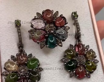 May include: A jewelry set featuring a ring and earrings with a floral design. The ring and earrings are adorned with colorful gemstones in shades of pink, green, and brown, set in a silver metal.