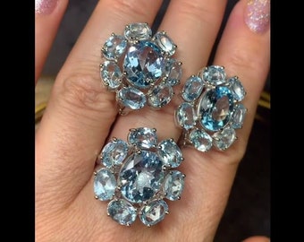 May include: Three silver rings with blue topaz gemstones set in a floral design. The rings are worn on a hand.