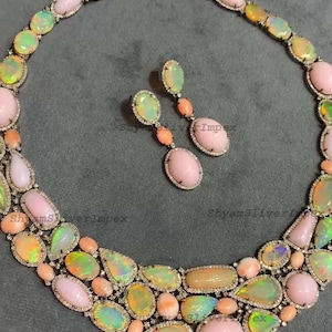 May include: A luxurious necklace and earring set featuring a variety of opal gemstones in shades of pink, green, and peach. The opals are set in a silver metal with a delicate diamond-like border. The earrings dangle with a matching design.