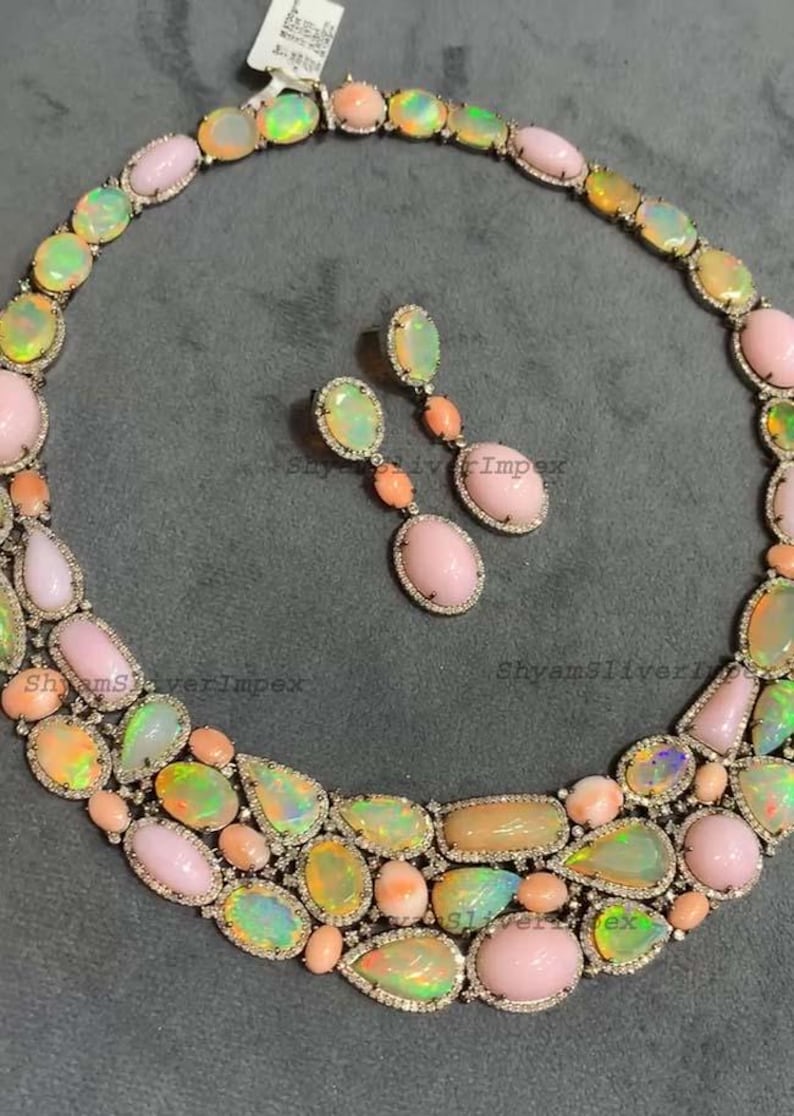 May include: A luxurious necklace and earring set featuring a variety of opal gemstones in shades of pink, green, and peach. The opals are set in a silver metal with a delicate diamond-like border. The earrings dangle with a matching design.