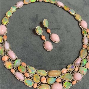 May include: A luxurious necklace and earring set featuring a variety of opal gemstones in shades of pink, yellow, and green. The jewelry is set in a silver metal with small, clear accent stones. The earrings have a drop design.